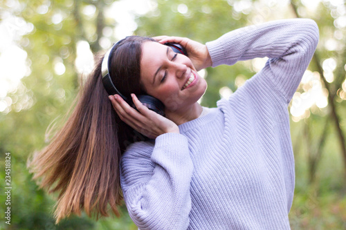 Caucasian european young woman or girl listening to music with helmets energetically and dancing moving her hair with energy in nature or very happy forest with closed eyes