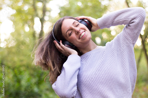Caucasian european young woman or girl listening to music energetically and dancing moving her hair with energy in nature or very happy forest with closed eyes holding helmets