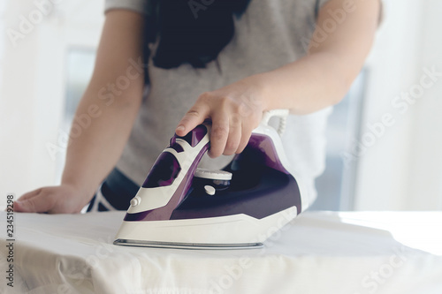 Woman's hand stroking the clothes steam iron on the background of the room.