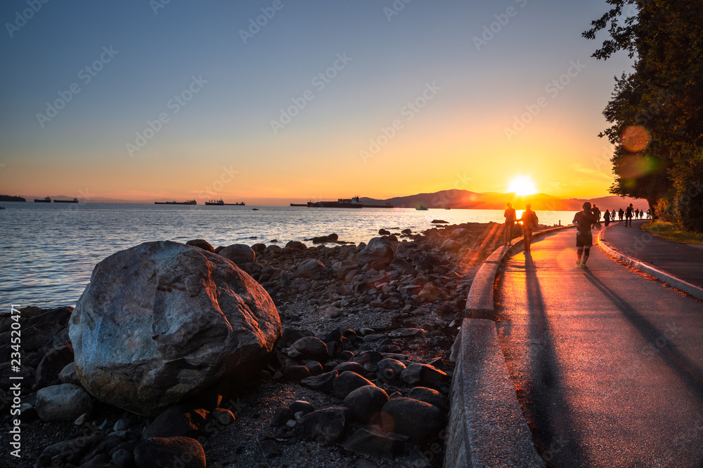 Fototapeta premium Ludzie na Seawall wzdłuż English Bay w Vancouver o zachodzie słońca. Flara obiektywu. Kolumbia Brytyjska, Kanada.