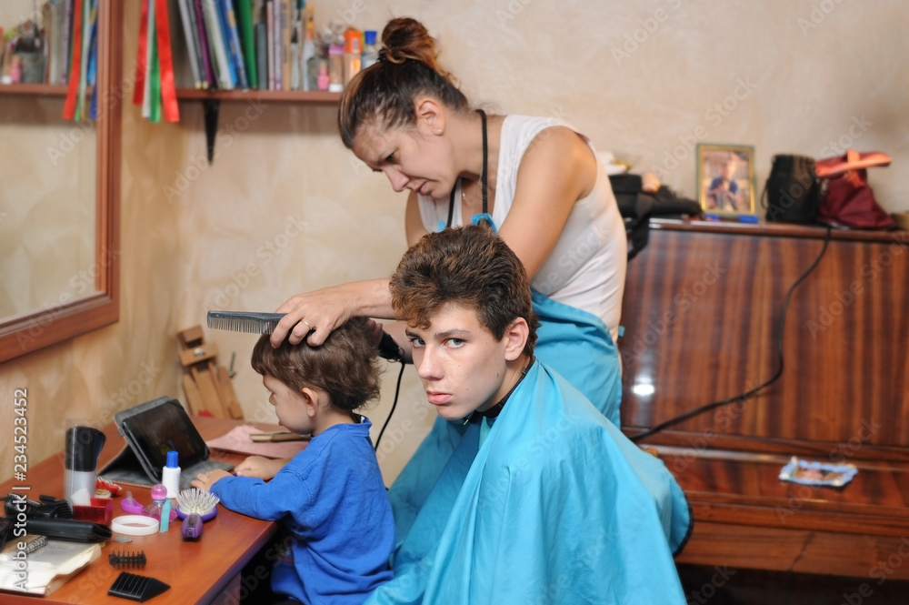 A woman works as a hairdresser at home. She cuts hair her sons with a  special hairdresser's model Stock Photo | Adobe Stock