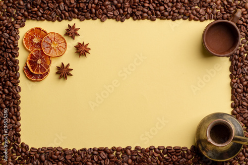 Conceptual coffee background. Yellow background, frame of coffee beans, slices of dried oranges and star anise. photo