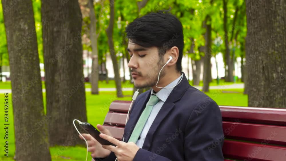 Asian businessman sitting in park and eating french fry in earphones
