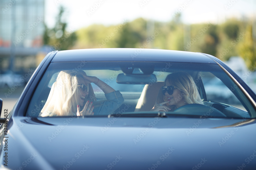 Image of young blondes sitting in black car in afternoon.