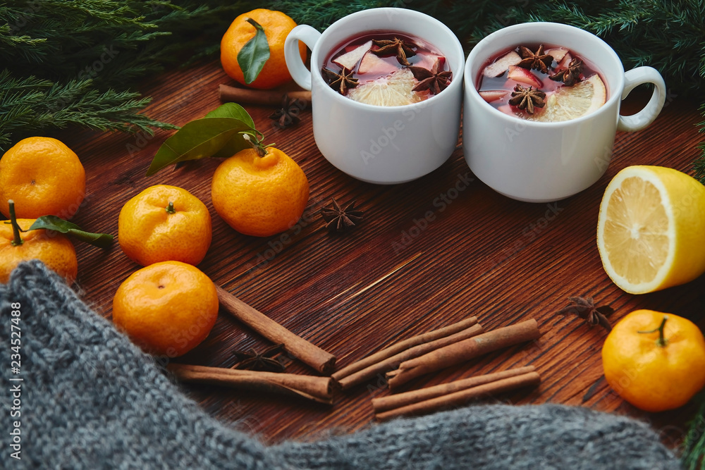 Christmas hot mulled wine in two small white cups with spices and citrus fruits on a wooden background and coniferous branches, top view