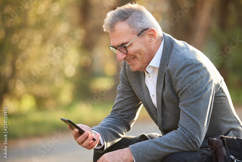 Business Mann schaut in sein Handy und sitzt im Grünen Park