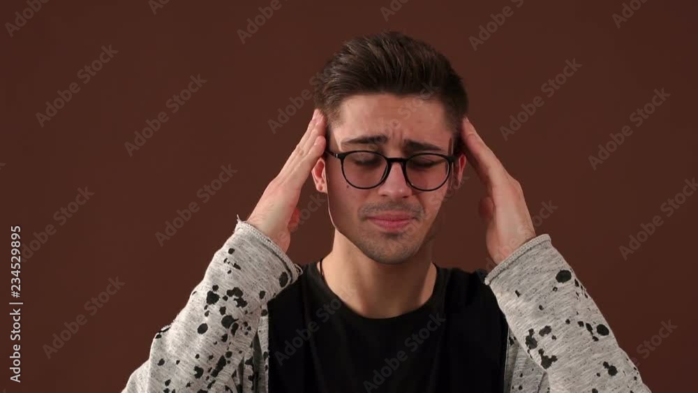 Handsome young man in glasses touching his head with hand feeling strong headache against the brown wall. Handsome young man in glasses touching his head with hand feeling strong headache against the brown wall.