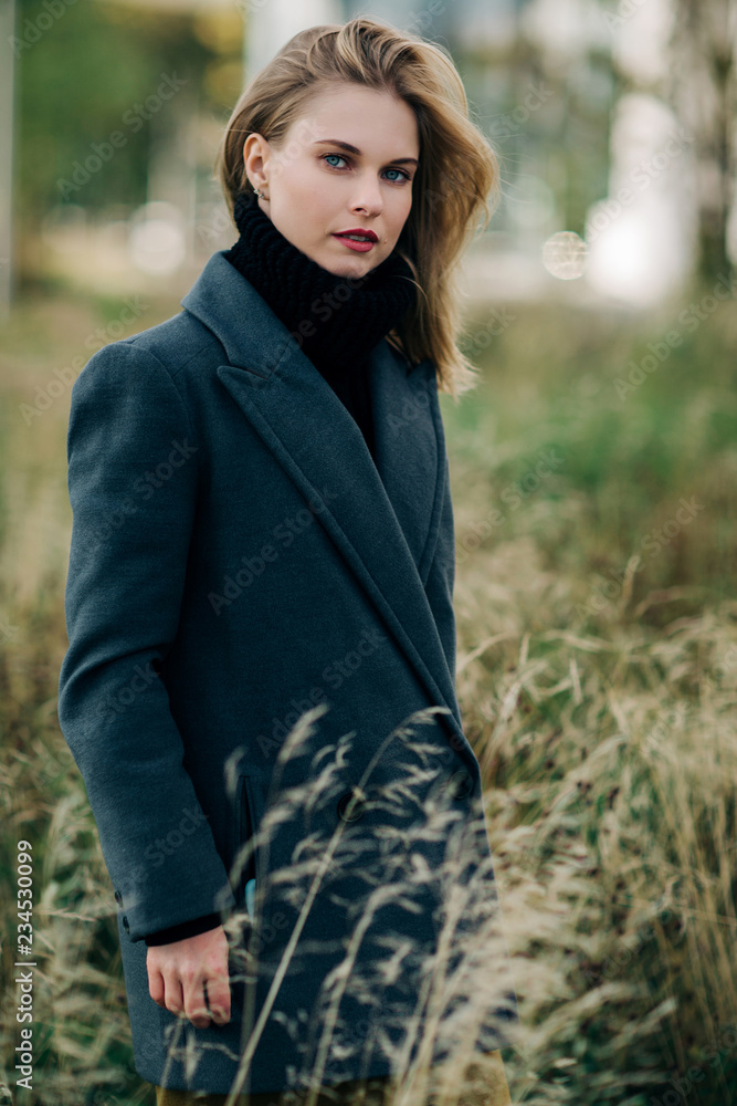 Portrait of young blonde in gray coat on blurred background of green trees Portrait of young blonde in gray coat on blurred background of green trees