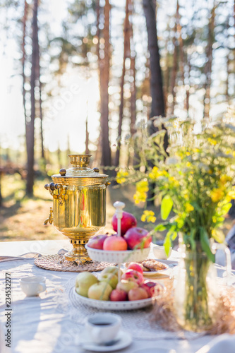 Traditional samovar on the table with apples and flowers outdoors