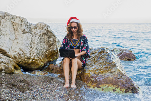 Workaholic young woman in a Santa hat working on the beach. photo