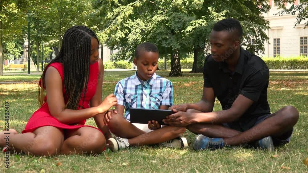 A young black family sits on grass in a park and works on a tablet A young black family sits on grass in a park and works on a tablet