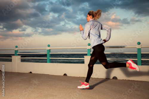 Blonde girl in sportswear running at seaside