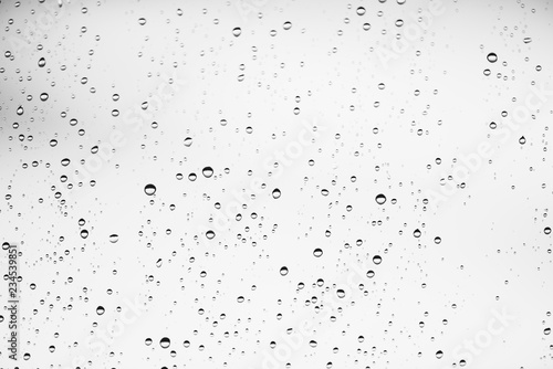Dirty window glass with drops of rain. Atmospheric monochrome light background with raindrops. Droplets and stains close up. Detailed transparent texture in macro with copy space. Rainy weather.