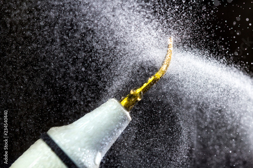 Dental ultrasonic scaler with water splash on black background. Close up.