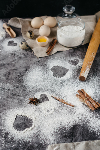 Healthy baking ingredients. Background with flour, rolling pin, eggs, and heart shape on kitchen gray kitchen table. Top view for Valentines day cooking. Copy space.