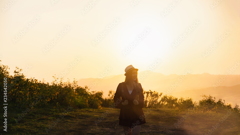 Asian woman travel holding backpack with sunset and flower fields.Front view of the young woman traveller.Travel alone concept.