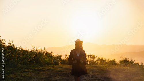 Asian woman travel holding backpack with sunset and flower fields.Front view of the young woman traveller.Travel alone concept.