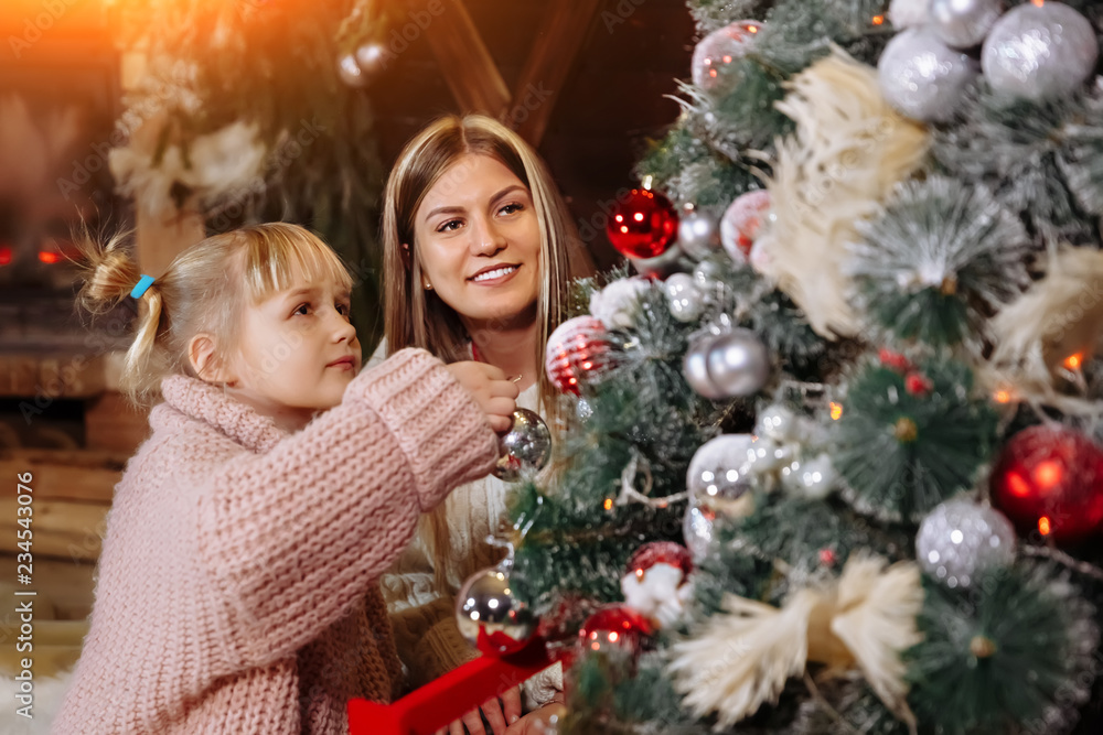 Merry Christmas and Happy New Year. Mom and daughter decorate the Christmas tree indoors. Loving family close up.
