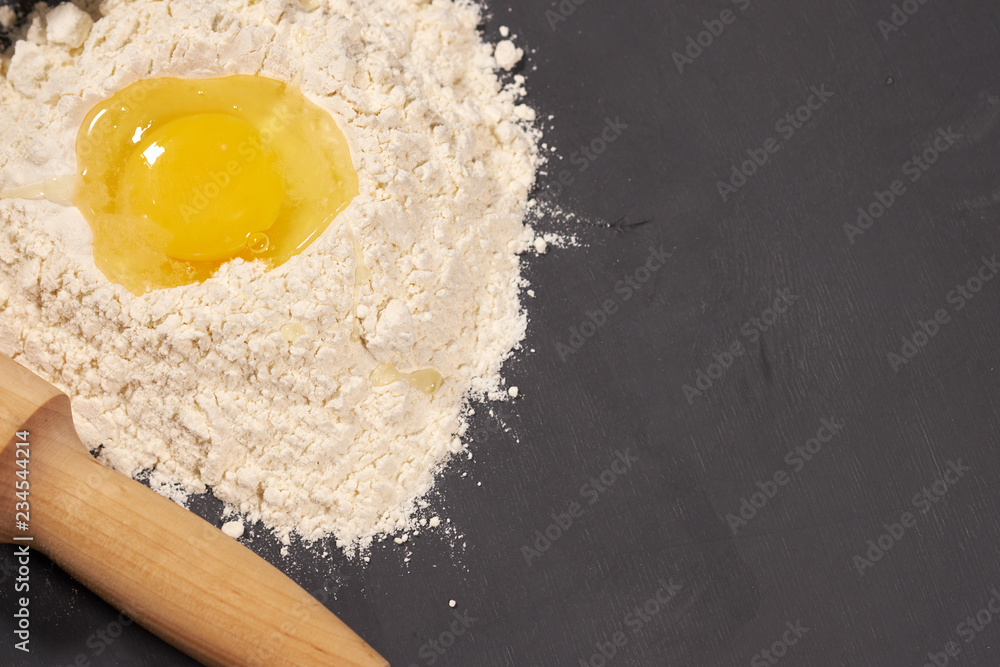 broken egg in flour, next to a rolling pin, selective focus broken egg in flour, next to a rolling pin, selective focus