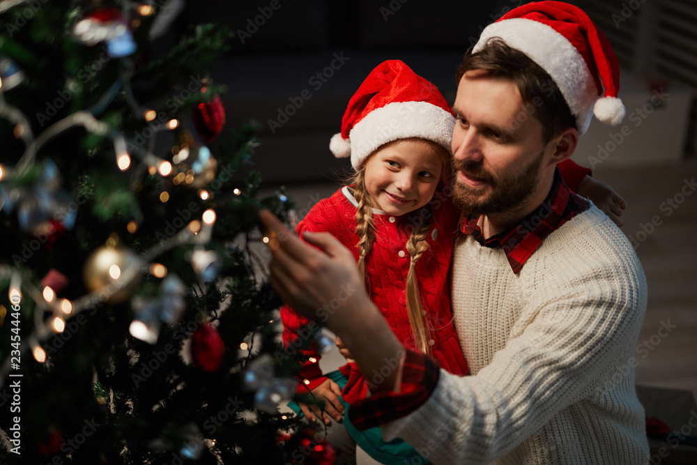 Young man and his little daughter decorating Christmas tree with toys and garlands Young man and his little daughter decorating Christmas tree with toys and garlands