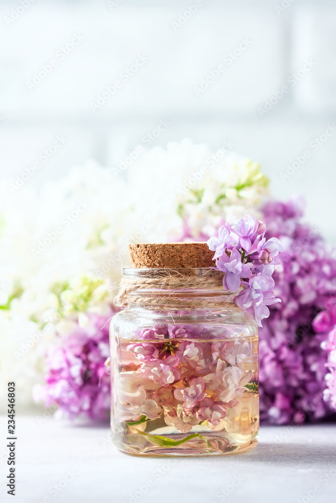 Naklejka Glass jar with aroma oil and with lilac flowers for spa and aromatherapy. Spa concept.