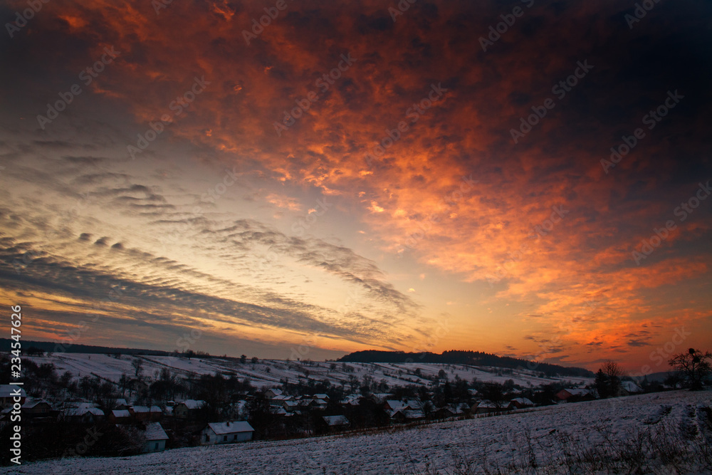 Colorful sunset in winter over hills forests in countryside village