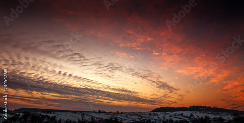 Colorful sunset in winter over hills forests in countryside village © okostia