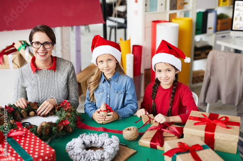 Happy little Santa girls and their pretty mother looking at you while preparing xmas stuff