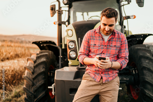 Portrait of smiling farmer using smartphone and tractor at harvesting. Modern agriculture with technology and machinery concept photo