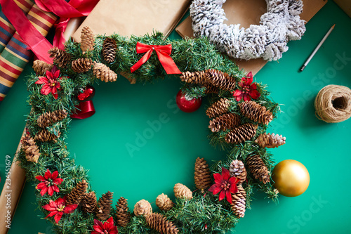 Christmas background with handmade coniferous wreath decorated with red flowers, bows and cones