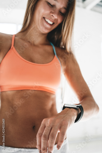 Photo fit woman after workout session checks results on smartwatch in fitness app..Sporty girl wearing sport tracker wristband arm. Vertical