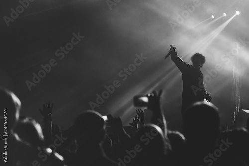Black and white photo of frontman silhouette in a stage backlights with hand with microphone raised up to the crowd of people