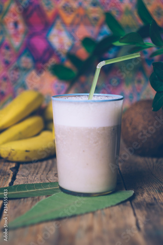 Banana smoothie (banana milkshake) on a wooden background with a bunch of bananas and green leaves. Healthy food concept
