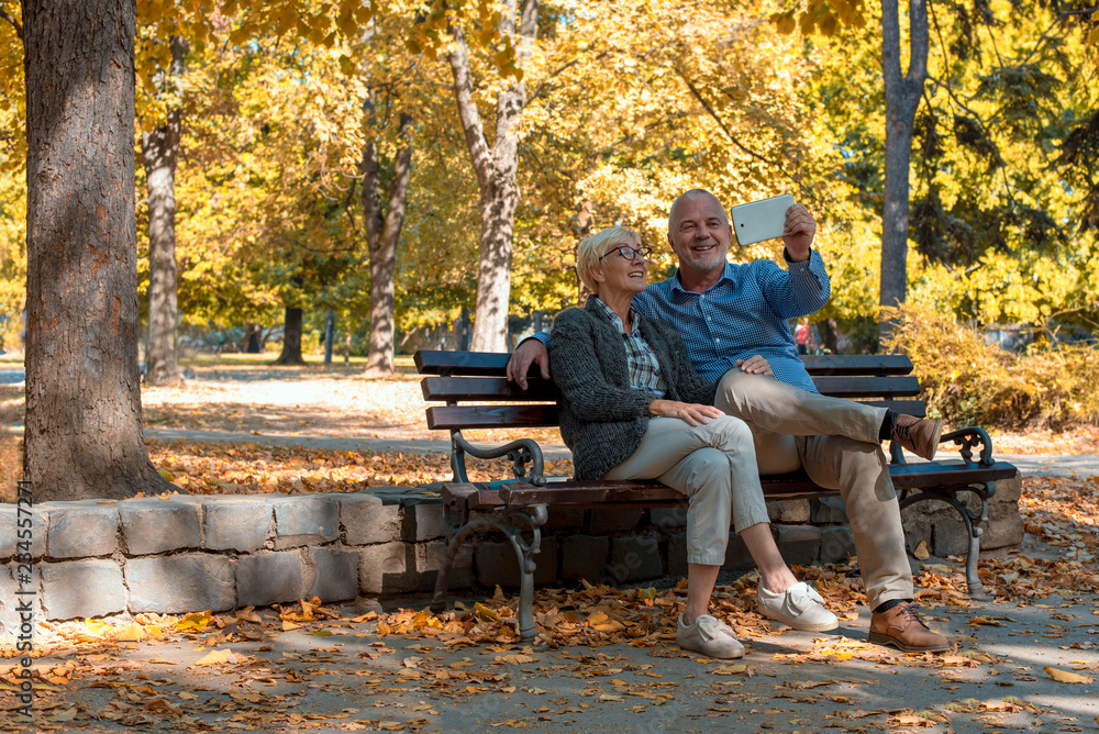 Beautiful smiling senior couple enjoying day together while taking selfie in autumn park Beautiful smiling senior couple enjoying day together while taking selfie in autumn park