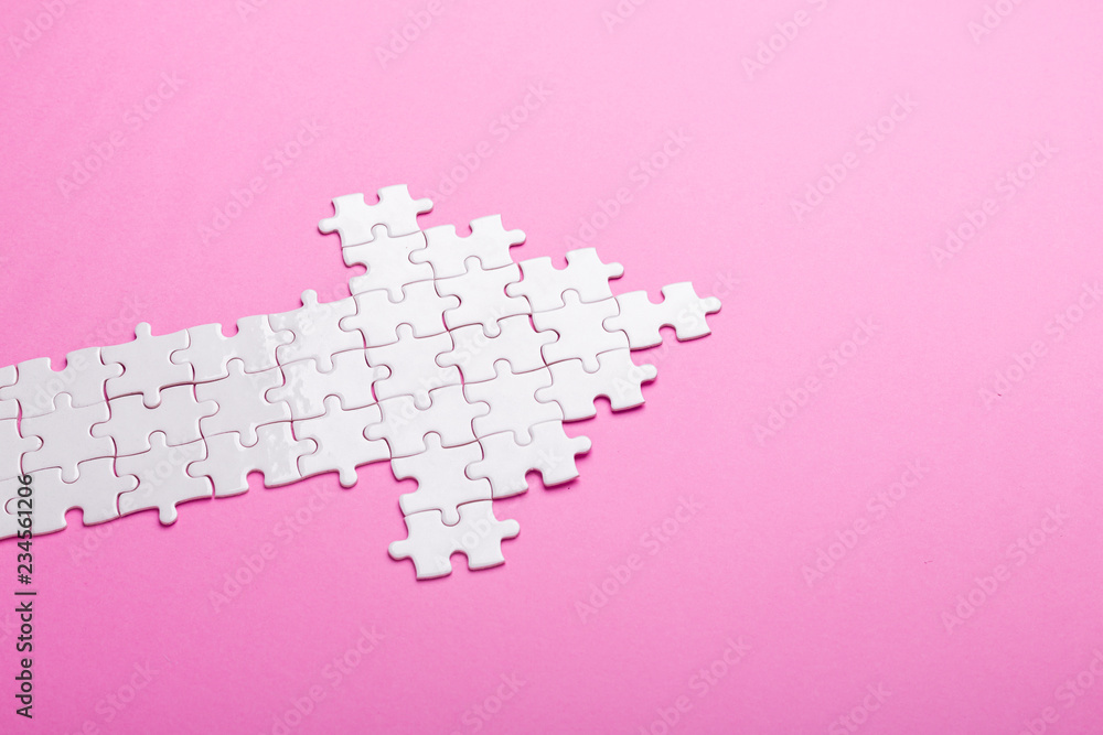 White puzzle. Arrow shape puzzle on pink background. Top view - obrazy, fototapety, plakaty 