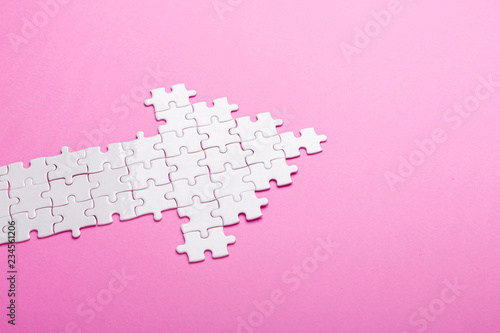 White puzzle. Arrow shape puzzle on pink background. Top view photo