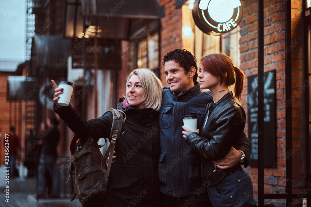 Cheerful friends standing together in an embrace near a cafe outside, looking away.