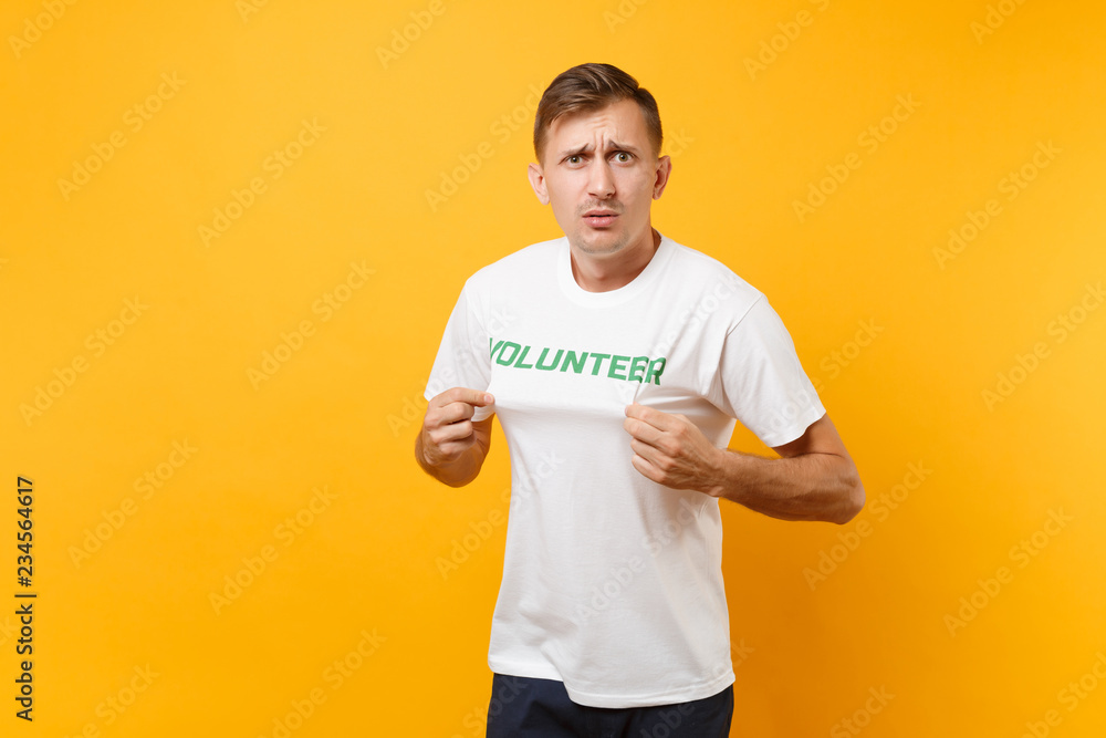 Portrait of fun shocked surprised young man in white t-shirt with written inscription green title volunteer isolated on yellow background. Voluntary free assistance help, charity grace work concept. Portrait of fun shocked surprised young man in white t-shirt with written inscription green title volunteer isolated on yellow background. Voluntary free assistance help, charity grace work concept.