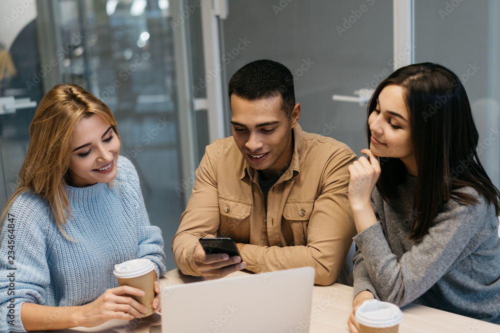 Group of multiracial hipster friends with emotional smiling faces using smartphone mobile app for mobile banking, shopping online, booking tickets. University students learning language together. Group of multiracial hipster friends with emotional smiling faces using smartphone mobile app for mobile banking, shopping online, booking tickets. University students learning language together.