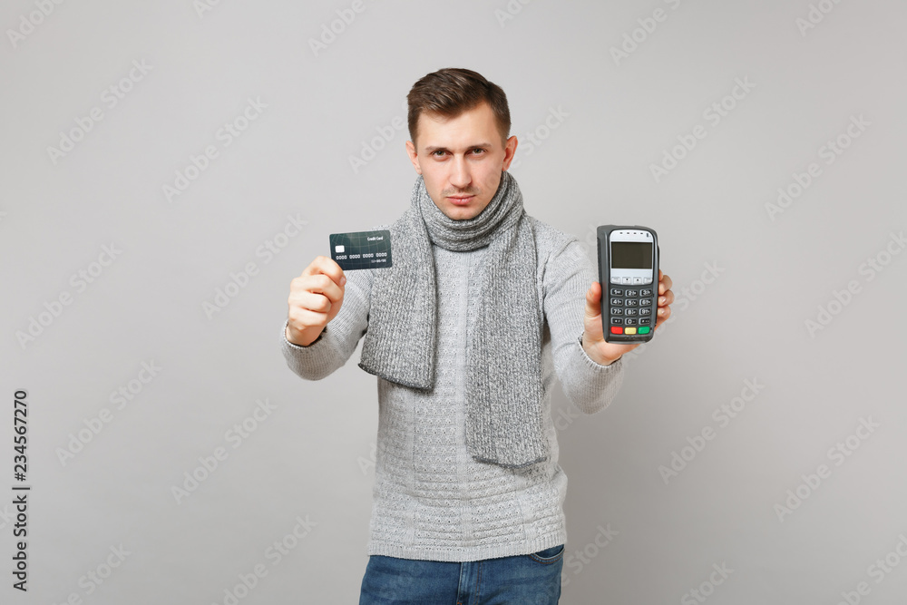 Serious man holding wireless modern bank payment terminal to process, acquire credit card payments isolated on grey background. Healthy fashion lifestyle, people sincere emotions, cold season concept. Serious man holding wireless modern bank payment terminal to process, acquire credit card payments isolated on grey background. Healthy fashion lifestyle, people sincere emotions, cold season concept.