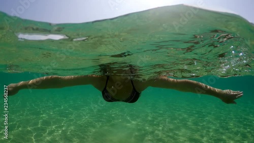 Underwater Low angle view of a young woman swimming on calm sea water surface backlit by summer sun shining rays photo