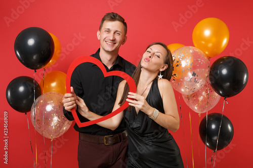 Loving couple in black clothes hold heart celebrating birthday holiday party isolated on bright red background air balloons. St. Valentine International Women Day Happy New Year 2019 concept. Mock up.