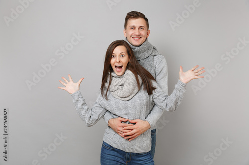 Young cute couple girl guy in gray sweaters, scarves together isolated on grey wall background, studio portrait. Healthy lifestyle, ill sick disease treatment, cold season concept. Mock up copy space.