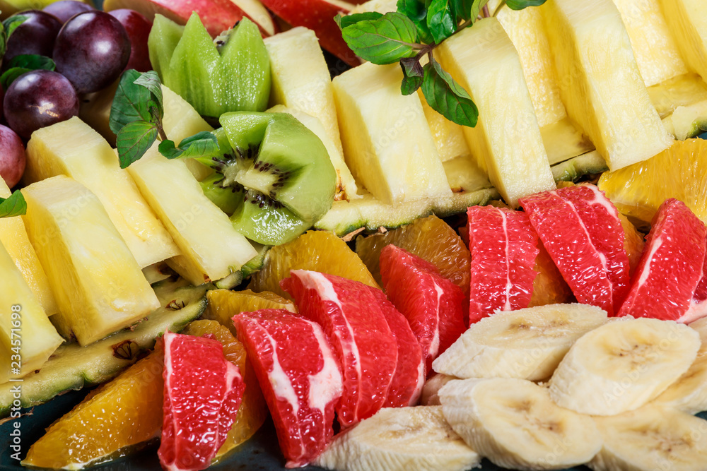 Assorted fresh fruits on plate. Apple, grapes, kiwi, pineapple, grapefruit, orange, banana and mint on wooden table. Selective focus Assorted fresh fruits on plate. Apple, grapes, kiwi, pineapple, grapefruit, orange, banana and mint on wooden table. Selective focus