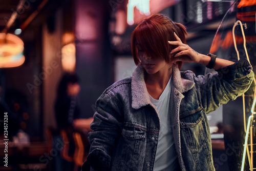 Stylish redhead girl standing in the night on the street. Illuminated signboards, neon, lights.