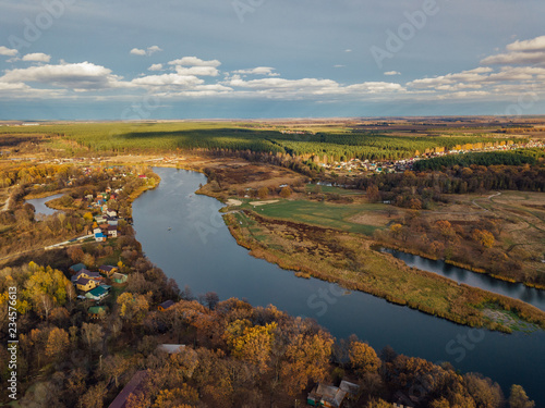 Aerial view of rural landscape in autumn. Small village houses  river  autumn trees  farm fields from drone point of view