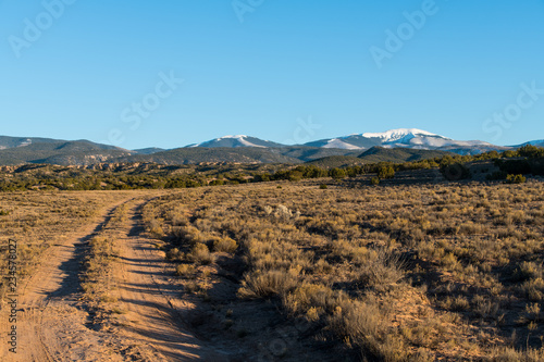 Dirt road curves through the high desert landscape toward the snow-capped Sangre de Cristo mountains near Santa Fe, New Meixco
