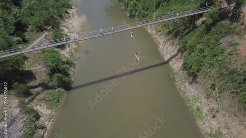 Aerial view of Suspension Bridge with the people walking across in Vietnam. Top view of Vietnamese river and two bamboo crafts under the bridge go adrift. 