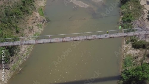 Aerial View of a tourist walking across the suspension bridge. Calm asian river on a summer day in Vietnam. Top view  