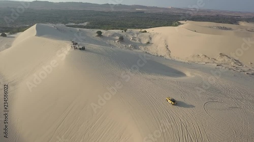 2K Aerial top view. Yellow jeep drives up to hill on sand dunes in Vietnam, Muine. Beautiful sunset time in the desert. Car trails in the sand.   
